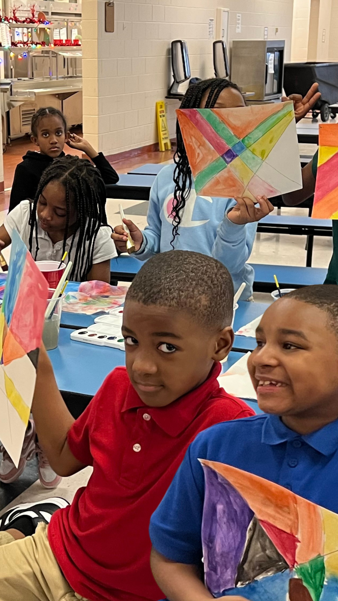 school kids in an art class holding up their colorful artwork on paper.